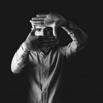 Black and white portrait of a man framing his face with his hands, creating an artistic, moody effect.
