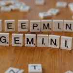 Wooden Scrabble tiles spelling 'Deepmind' and 'Gemini' on a wooden surface, a concept of AI and games.