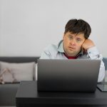 Person with Down Syndrome sitting at a desk, working on a laptop indoors.